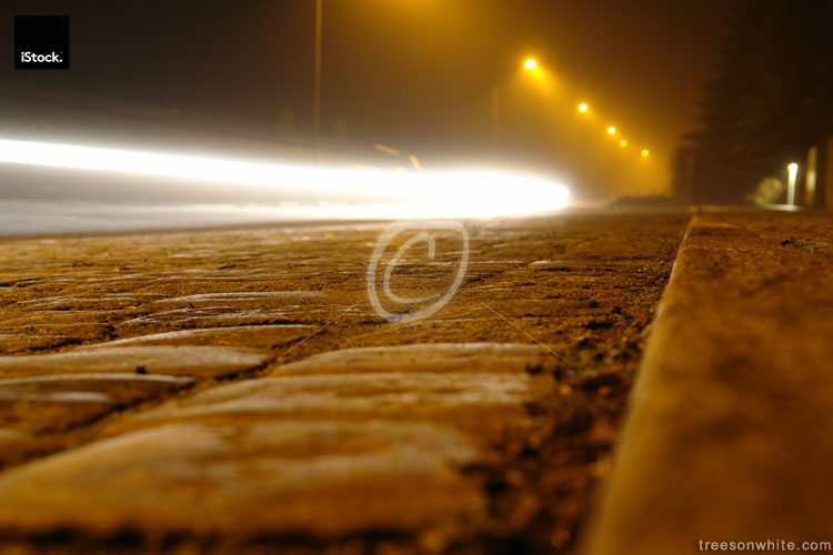 Foggy street at night with car driving by.